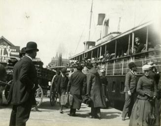 Image shows some people on the boat and some walking on the Harbour.
