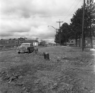 Image shows a car parked by the site. There are some building in the background.