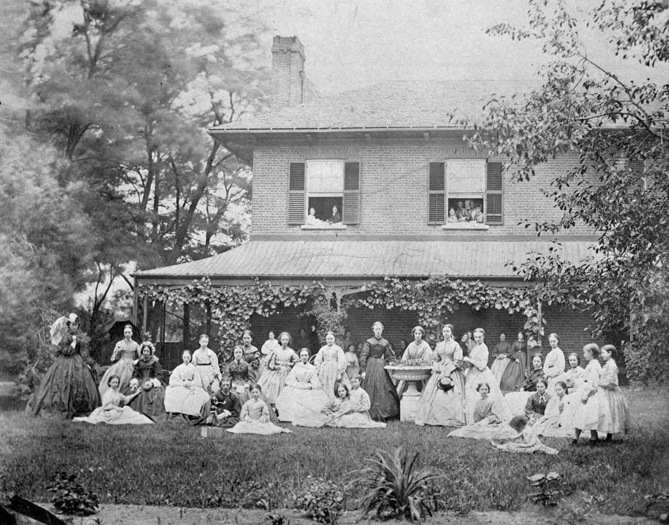 Black and white photograph of a group of thirty-nine 19th-century individuals, some women, a fe…