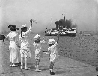 Image shows a lady and three girls at the Harbour waving to the leaving boat.