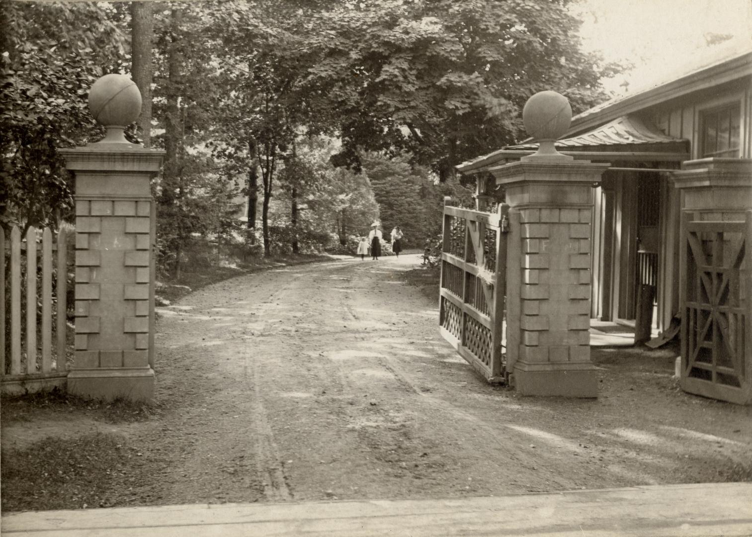 Image shows open gates leading along the road with lots of trees around.