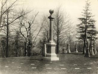 Image shows a cemetery monument with some trees and other monuments around.