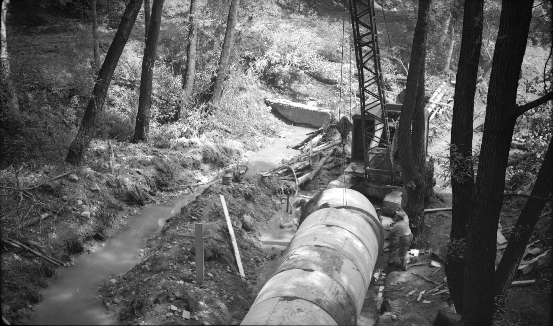 Image shows a few pipes on the ground and some construction equipment.