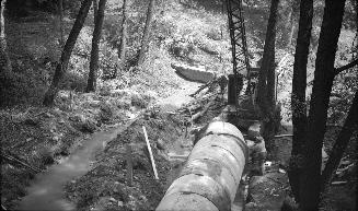 Image shows a few pipes on the ground and some construction equipment.