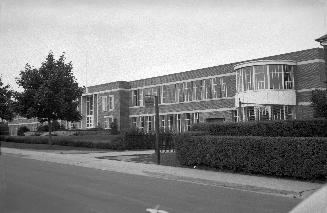 Image shows a street view with a two storey school building along it.