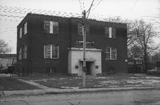 Image shows a small two storey school building from the front along the street.