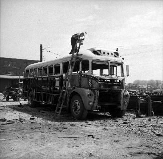 Image shows a person working on the top of the bus by standing on the ladder.