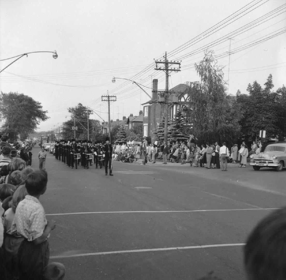 Image shows participants of the parade marching along the street with some spectators cheering  ...