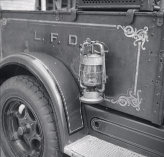 Image shows a part of a vehicle that includes a wheel, a lamp and a step.