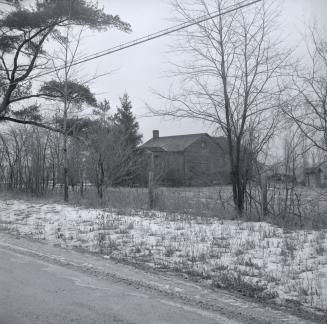 Image shows a street with a some trees and a house in the background.