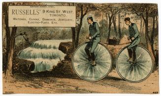 Two men riding on a tandem bicycle with very large wheels (like a penny farthing). They are rid ...