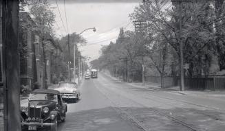 Image shows a street view with a streetcar on the tracks and a few cars parked on the left side ...
