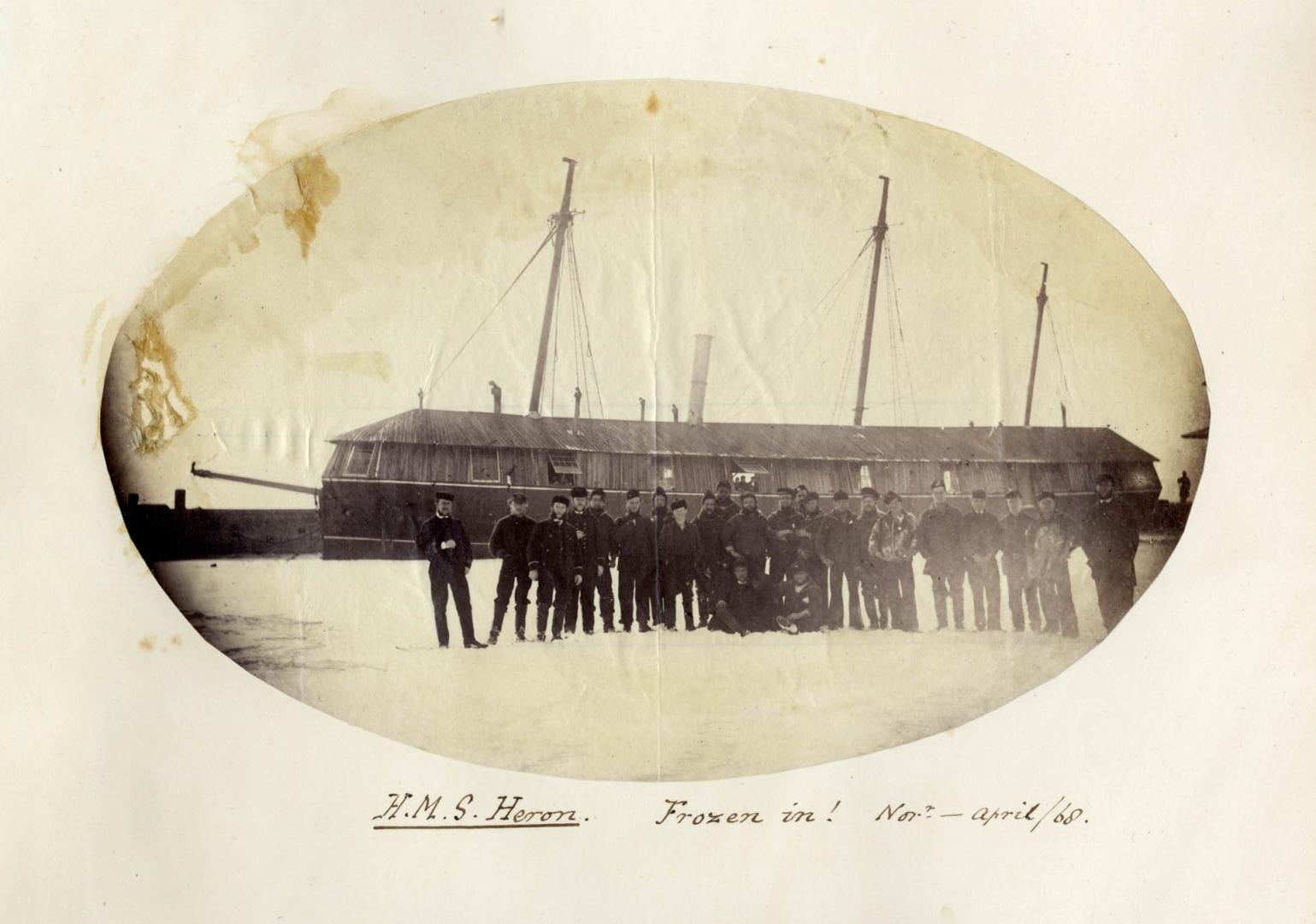 Image shows a group of people posing for a photo with a gunboat behind them.