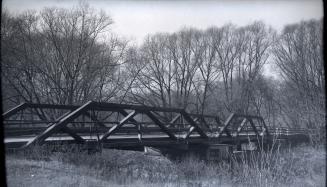 Image shows a bridge across the river with a lot of trees in the background.