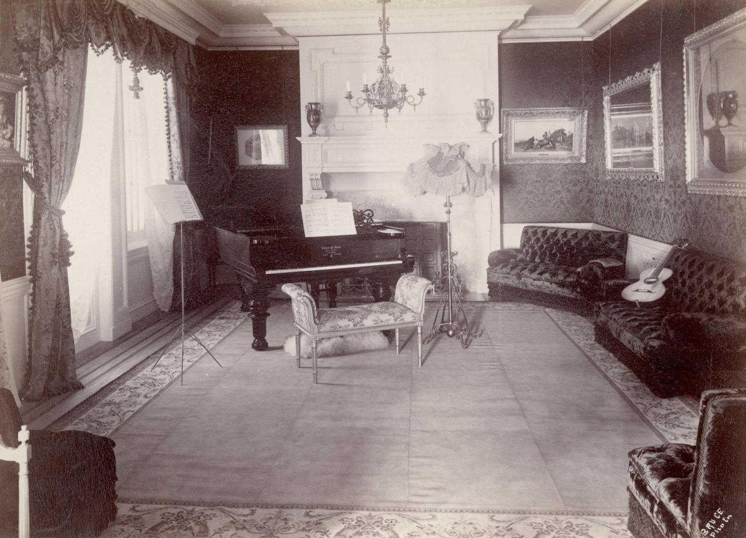 Image shows a music room that has a baby grand piano, music stand and a few couches.