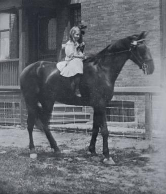 Image shows a girl riding a horse by the building.