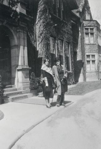 Image shows a lady and a gentleman posing for a photo on the sidewalk by the building. 