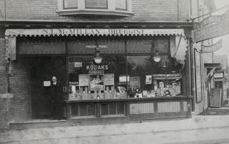 Image shows the front of a drug store that reads "N. L. McMillan Druggist".
