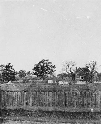 Image shows a fence and a house and some trees in the background.