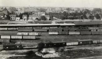 Image shows an aerial view of the railway yards with some buildings in the background.