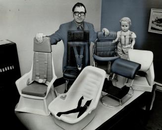 George Ham of the Ontario Safety League surveys some of the child car seats and restraints that the league recommends for use by Canadians. The doll on the right is wearing a safety harness