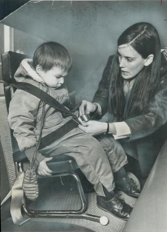 David Moorhouse, 2, looks on with interest as Judy Thomson of the Ontario Safety League straps him into a car safety seat. The seat, made in Montreal (...)