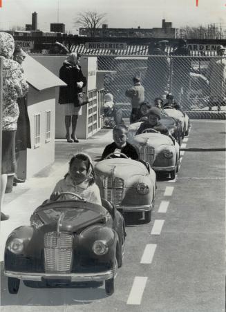 Midget motorists in pedal cars are being taught the basic rules of traffic safety in a model village in a shopping centre parking lot at Don Mills Rd.(...)