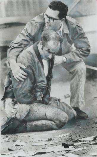 Injured when a bank robber was blown to bits by his own bomb, Constable Don Milliard sits in a Kenora street, comforted by Constable Ken Richardson an(...)