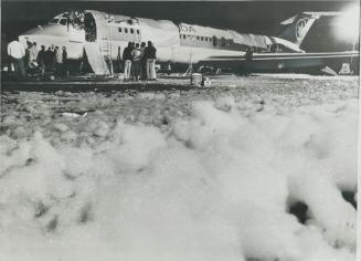 Investigative teams, including FBI agents, check out the fire-gutted DC-9 as it lies on the runway surrounded by fire-retardant foam