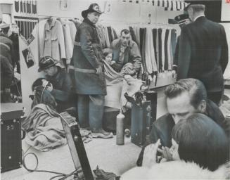 Firemen equipped with oxygen masks and stretchers set up a field hospital in a dress shop to treat victims of a mysterious gas which knocked out emplo(...)