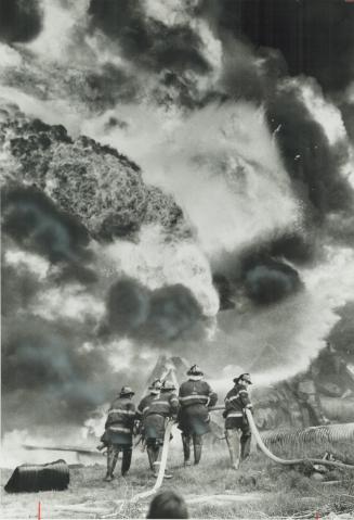 Firemen work close to the blazing inferno with a large watergun, keeping streams of cooling water on three tank cars of acetone on a railway siding ne(...)