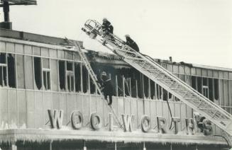 Cooling the ashes. Scarborough firemen hose down still-glowing embers after a two-alarm fire above a Woolworth store at Eglinton Ave. E. and Brimley R(...)