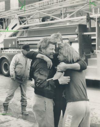 Grieving family members comfort each other outside their burning home on Carlaw Ave