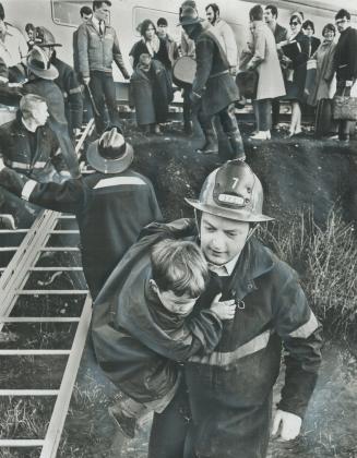 Rescued from sabotaged train, youngster clings with his arms around shoulders of Etobicoke fireman James Grant, as he is carried to safety from scene (...)