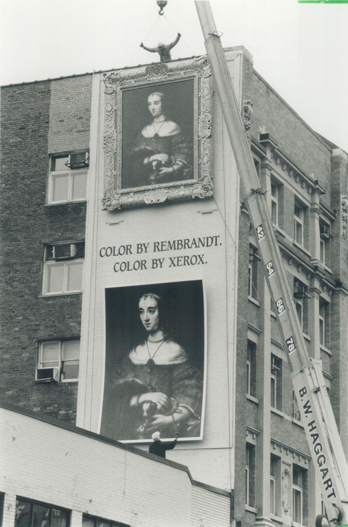 Tall order. Workers hoist and hang a reproduction of Rembrandt's Lady Petting Lap Dog on a building near Yonge and Bloor Sts. yesterday. The replica p(...)