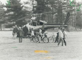 A group of men looking at a grounded helicopter, alongside kids on bikes