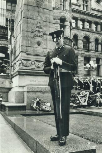 A man in uniform stands, with bowed head, in front of the cenotaph at Old City hall, which read ...