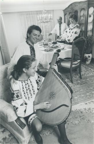 Ukrainian Christmas: Lisa Machula, 14, plays the bandula for her brother Taras, 23, while their parents Raisa and John prepare for their traditional Christmas Eve dinner
