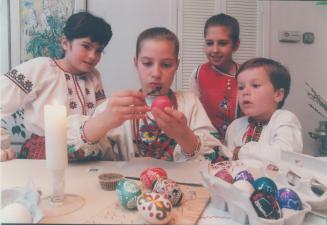 Young children in traditional clothing painting eggs with intricate colourful designs