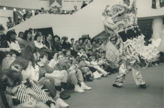 A dancer wearing a large, stylized Chinese Dragon head costume performs for a group of children ...