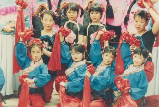 Girls in traditional matching vibrant clothing posing together with one arms raised holding red ...