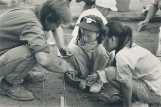 Digging in: Teacher Ron Postill (right front) pitchs in with pupils in a dig at Leslieville Public school as archeologists stand by to identify their finds