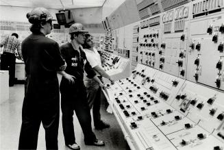 Workmen check fueling rods on reactor under construction, above