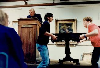 Above left, an antique table is hoisted onto the auction block by helpers at a Deveau auction