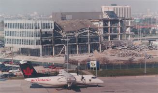 Shows an Air Ontario air plane in front of a partially-demolished building.