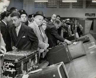 Arrivals crowd to counter seeking their luggage