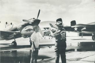 World War II Planes (p-40 fighter left and B-25 bomber) form a backdrop as youth and age discuss flying at Harlingen