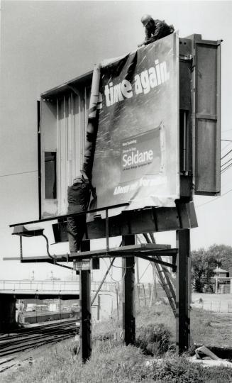 Easy as one, two three . . . Francis Andrade, bottom, and Louis Guinho, top, install a new display on a transparency-type billboard measuring 3 metres(...)