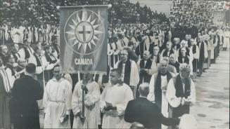 Faces of the Anglican Congress watch a phalanx of Canadian clergymen, left, making an impressive sight as they entered Maple Leaf Garden for the openi(...)
