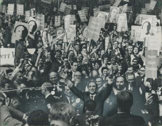 Amid convention bedlam Pierre Elliott Trudeau stands with arms extended above his head against a roaring sea of cheering delegates and waying placards(...)